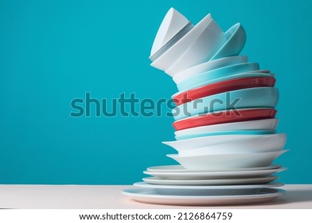 Unstable stack of many dishes on light blue background