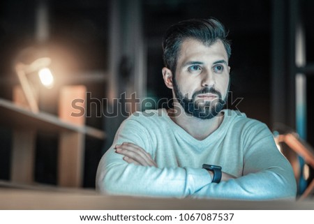 Unstoppable progress. Musing reflective adorable man looking aside while crossing arms and posing on blurred background