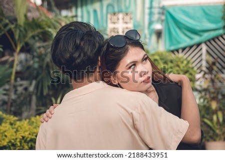 An unsure asian woman hugs her partner faking forgiveness or showing doubt. An emotionless face concealing her inner conflict. Outdoor scene. Stock photo © 