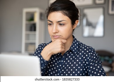 Unsure Indian Business Woman Sit At Desk Looks At Laptop Screen Thinking Over Task Do Research Analyzing Results Feels Doubtful. Concentrated Serious Office Worker Cogitating Making Decision Concept