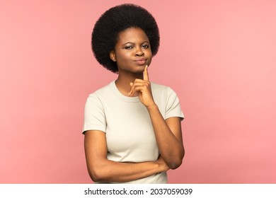 Unsure pensive young african american student woman touching her chin, frowning, pondering, look at camera doubtfully, plans or reconsiders something, feeling hesitant isolated on studio pink wall 