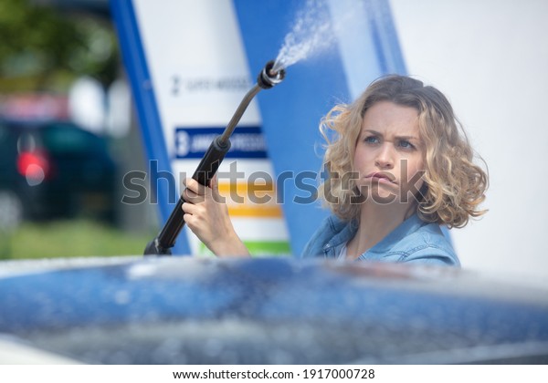 unsure woman\
standing with spray foam to clean\
car