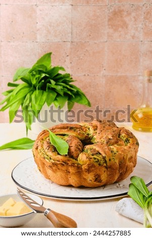 Unsweetened pastries, round snack twisted bread with wild garlic pesto on a white dish on a light concrete background. Ramson recipes. Unsweetened baked goods