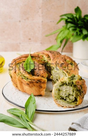 Unsweetened pastries, round snack twisted bread with wild garlic pesto on a white dish on a light concrete background. Ramson recipes. Unsweetened baked goods