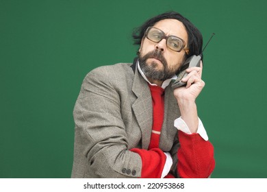 An untidy bizarre man, wearing big patched glasses and a toupee, trying to answer an incoming phone call on an antique big cellphone, over green background