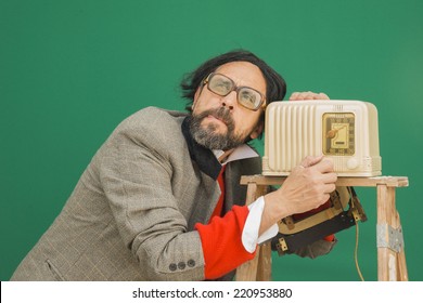 An untidy bizarre man, wearing big patched glasses and a toupee, listening to a station on an antique bakelite tube radio on a ladder, over green background 