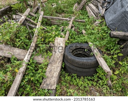 An unused car tire discarded amongst a pile of wood and weeds.