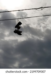 unusual backlit vision of some shoes dangling from electric wires - Shutterstock ID 2199709307