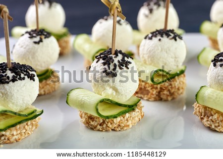 An unusual beautiful appetizing appetizer for a festive table. Mini canapes from a piece of baguette with sesame, thin slice of cucumber and a ball of cheese. Exotic black sesame for decoration.