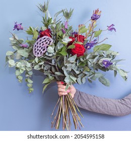 Unusual Bouquet On Blue Background. Square. Woman Gives Bouquet For Man. Concept Of Creative Floristry