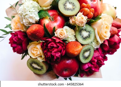 An unusual bouquet of peonies, roses, strawberries, kiwi and apples on white. Top view. Close up