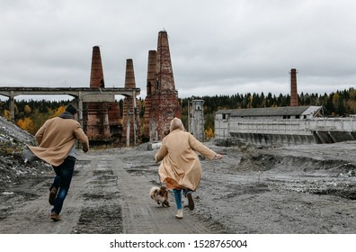 unusual couple in love in a brown coat with a dog running and cuddling in an abandoned city against a background of destroyed brick ovens of a factory, autumn travel to the north of Russia, apocalypse - Powered by Shutterstock