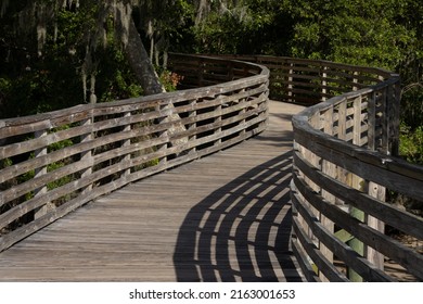 Unusual interesting winding wooden bridge dock or deck with shadows from the curved railing leading into the trees on a sunny afternoon