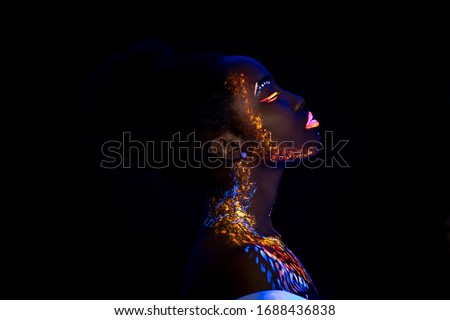 unusual portrait of beautiful african fashion woman in neon UF light. attractive young model girl with fluorescent creative psychedelic make-up, body-art