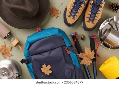 Unveiling autumn's majesty through hiking. Top view shot of metal utensils, hat, bottle, boots, bag, trekking sticks, cones, autumn leaves on green background - Shutterstock ID 2366534379