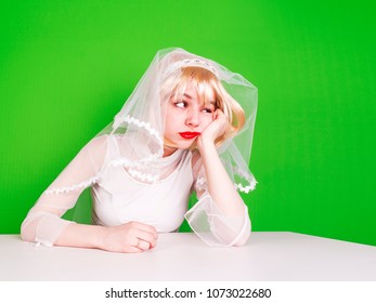 Unwanted Marriage, Bad Life Decisions Concept. Serioos Bride Wearing White Dress Sitting At Table And Waiting For Wedding, Isolated On Green.