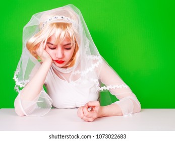 Unwanted Marriage, Bad Life Decisions Concept. Serioos Bride Wearing White Dress Sitting At Table And Waiting For Wedding, Isolated On Green.