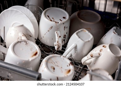 Unwashed, dirty dishes in dishwasher. Mess in the kitchen. Dirty kitchenware, plates and mugs. Messy dishware. Close up view.