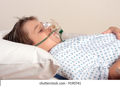 An Unwell Child Resting Wearing A Patient Gown Has An Oxygen Mask, Inhaler On His Face.