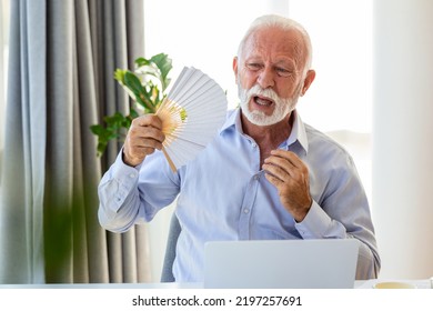 Unwell Senior Business Man Sit On Desk Work On Laptop Wave With Hand Fan. Overheated Man Worker Use Waver Suffer From Heatstroke In Office, Struggle With No AC At Workplace.