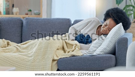 Unwell woman with period cramps on a couch at home. Female experiencing discomfort or belly ache from PMS or menstruation cycle. Female trying to sooth painful endometriosis with a hot water bottle