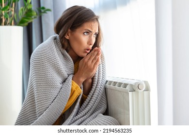 Unwell woman renter in blanket sit in cold living room hand on old radiator.suffer from lack of heat . Unhealthy young woman struggle from chill freeze at home. No heating concept. - Shutterstock ID 2194563235