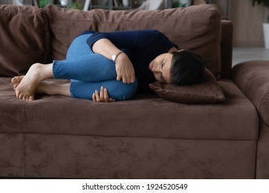 Unwell young Indian woman lying on sofa at home have stomachache suffer after miscarriage or abortion. Unhealthy depressed ethnic female struggle with bad painful feeling. Health problem concept.