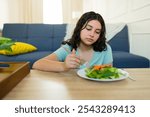 Unwilling teenage girl eating a healthy salad at home, grappling with eating disorder and health issues, highlighting the connection between diet and mental health