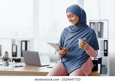 Unwind At Work. Young Saudi Businesswoman In Hijab Drinking Coffee And Using Digital Tablet, Relaxing In Office, Free Space - Powered by Shutterstock