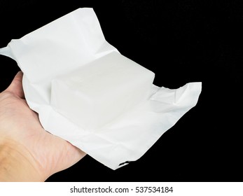 Unwrapped Block Of Coconut Fat In Aluminum Paper Held By A Person, Towards Black