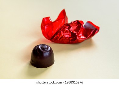 An Unwrapped Chocolate Cherry Bonbon With The Wrinkled Red Wrapping Paper And Isolated On A Yellow Background.