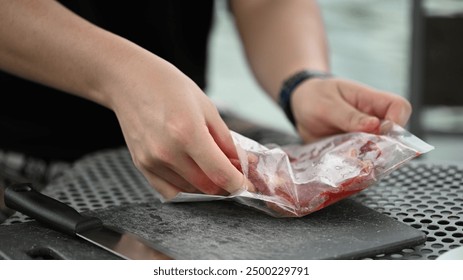 Unwrapping Fresh Ingredients, A close-up of hands opening a vacuum-sealed bag of fresh meat by a tranquil lakeside, the outdoor culinary preparation. - Powered by Shutterstock