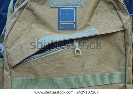 The unzipped back pocket of a men's military khaki backpack with cloth on the shoulders of a tourist during the day on the street