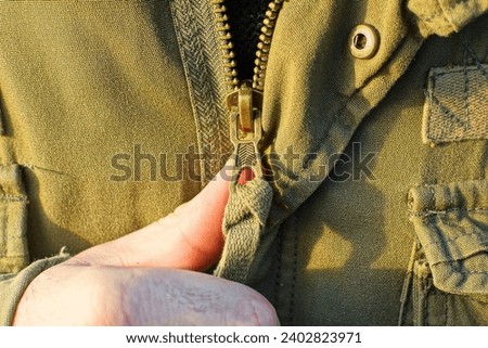 unzipped iron yellow fashionable modern new zipper with unbuttoned iron button on military winter olive colored stylish jacket fabric and finger of hand Foto d'archivio © 
