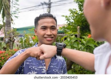 An upbeat Filipino man fist bumps his friend while outside. Showing respect or support. Gen Z generation.