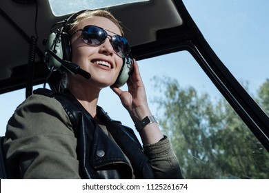 Upbeat mood. Beautiful helicopter pilot smiling cheerfully while listening to air traffic controller in her headphones