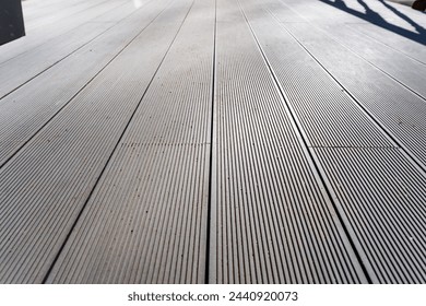 An upclose photo of a grey wooden deck with a diagonal pattern. The flooring is made of hardwood planks, possibly a composite material, stained to match the road surface next to it