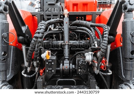 An upclose view of the front of a red and black tractor, showcasing its motor vehicle engineering with visible nuts, machine parts, plumbing valves, and automotive supercharger parts
