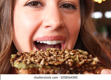 Upclose view of pretty woman smiling and eating taking a bite out of avocado toast looking into camera, horizontal shot