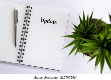 UPDATE. Single Creative Word On A Notepaper Book. Flat Lay Concept With Open Book Page, Pen And Green Plant On White Table Background. Reminder For Updating Business Progress, Website And Contents.