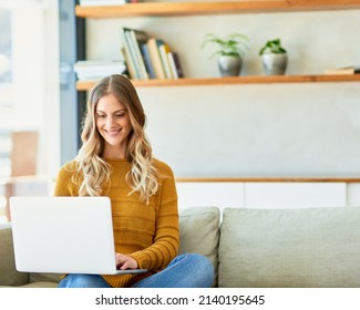 Updating her blog. Shot of an attractive young woman using her laptop while sitting on the sofa at home.