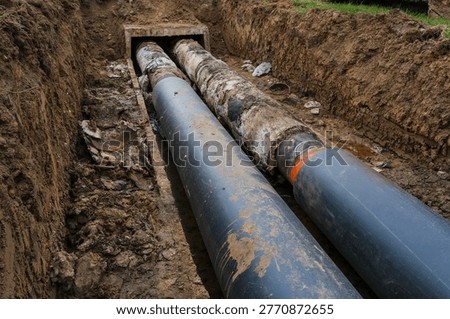 Upgrade of district heating system with transition from old worn insulation to modern insulated pipes. Excavation trench with utility repair works highlighting energy efficiency and infrastructure modernization process.