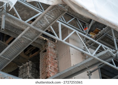 Uplifting angle on complex construction site with robust metal scaffolding, highlighting exposed elements of old building undergoing significant renovation and structural work.