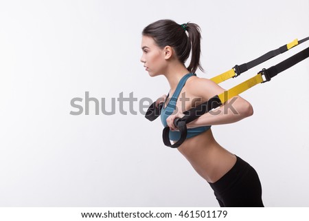 Upper body exercise concept. Beautiful woman exercising with suspension straps alone in studio. TRX concept isolated on white background.