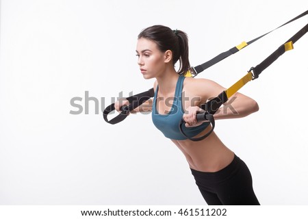 Upper body exercise concept. Image of beautiful woman exercising with suspension straps alone in studio. TRX concept isolated on white background.