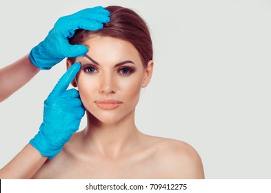 Upper eyelid blepharoplasty. Beautiful middle age woman getting ready for eyelid lift plastic surgery doctor hands in blue gloves point fingers to her eye on white. Beauty, people and health concept