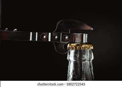 Upper part of the glass beer bottle with metal can opener on the black background