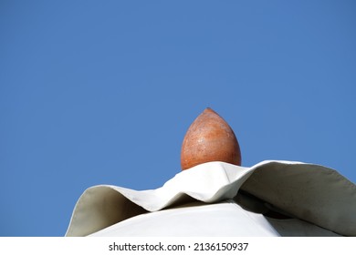 The Upper Part Of The Pole Is Made Of Wood And White Tarpaulin Against The Blue Sky. It Is A Large Outdoor Umbrella.