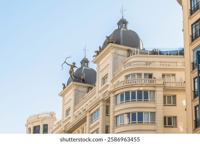 Upper portion of a building located on Gran Via, 31 in Madrid, Spain. Rooftop is adorned with statues of archers and decorative elements, adding a striking artistic touch to the building architecture