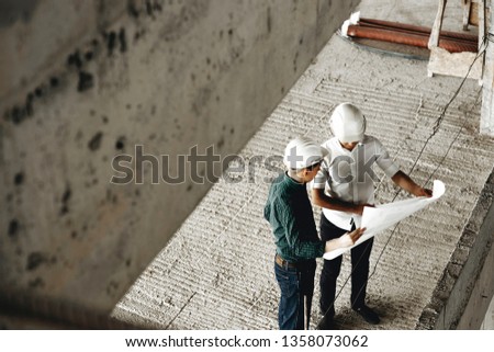 Upper view of a adult arhitecht and his worker talking about building in constructiion being on the worksite.